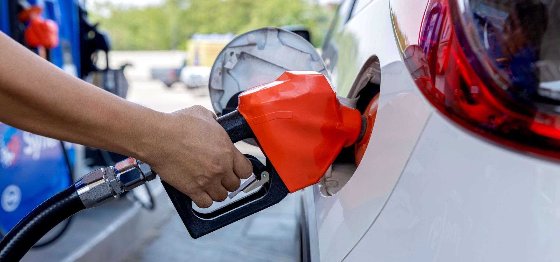 a hand on a gas pump fueling a white car